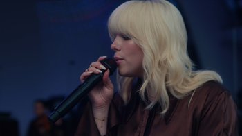 Movie still from “Happier Than Ever: A Love Letter to Los Angeles” (2021), directed by Patrick Osborne – A woman with blonde hair is holding a microphone; Close Up shot, Low angle