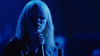 Movie still from “Happier Than Ever: A Love Letter to Los Angeles” (2021), directed by Patrick Osborne – A woman holding a microphone in her hands; Close Up shot, Low angle