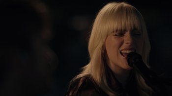 Movie still from “Happier Than Ever: A Love Letter to Los Angeles” (2021), directed by Patrick Osborne – A woman singing into a microphone in front of a crowd of onlookers; Close Up shot, Over the shoulder angle