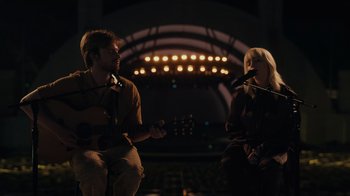 Movie still from “Happier Than Ever: A Love Letter to Los Angeles” (2021), directed by Patrick Osborne – A man and a woman are playing guitar and singing; Wide shot, High angle