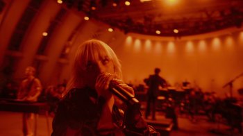 Movie still from “Happier Than Ever: A Love Letter to Los Angeles” (2021), directed by Patrick Osborne – A woman holding a microphone in front of a crowd; Extreme Wide shot, Low angle