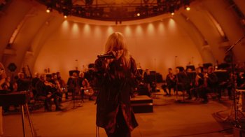 Movie still from “Happier Than Ever: A Love Letter to Los Angeles” (2021), directed by Patrick Osborne – A woman singing into a microphone in front of an orchestra; Wide shot, Low angle