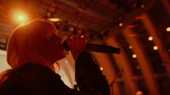 Movie still from “Happier Than Ever: A Love Letter to Los Angeles” (2021), directed by Patrick Osborne – A woman is singing into a microphone in the dark; Close Up shot, Low angle