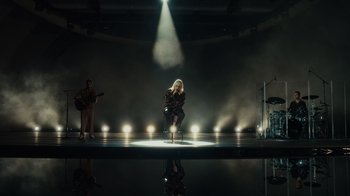 Movie still from “Happier Than Ever: A Love Letter to Los Angeles” (2021), directed by Patrick Osborne – A woman sitting on a stage with a microphone; Extreme Wide shot, High angle
