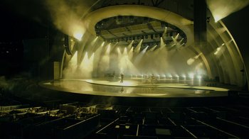 Movie still from “Happier Than Ever: A Love Letter to Los Angeles” (2021), directed by Patrick Osborne – A stage lit up with lights in a large room; Extreme Wide shot, High angle