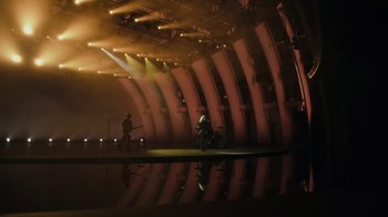 Movie still from “Happier Than Ever: A Love Letter to Los Angeles” (2021), directed by Patrick Osborne – A person riding a bike inside a building with lights on; Extreme Wide shot, High angle