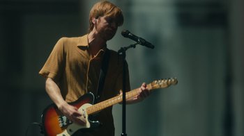 Movie still from “Happier Than Ever: A Love Letter to Los Angeles” (2021), directed by Patrick Osborne – A man with a guitar and a microphone in front of him; Medium shot, Low angle