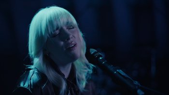 Movie still from “Happier Than Ever: A Love Letter to Los Angeles” (2021), directed by Patrick Osborne – A woman singing into a microphone in front of a microphone stand; Close Up shot, Low angle