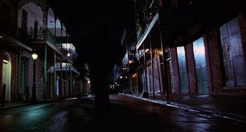 Movie still from “Hard Target” (1993), directed by John Woo – A dark street with lights and buildings on both sides of the street; Extreme Wide shot, Low angle