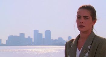 Movie still from “Hard Target” (1993), directed by John Woo – A woman standing on a beach with a city in the background; Close Up shot, Over the shoulder angle