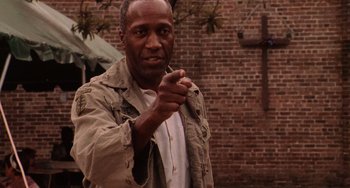 Movie still from “Hard Target” (1993), directed by John Woo – A man in a tan jacket pointing at the camera; Medium shot, Low angle
