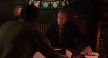 Movie still from “Hard Target” (1993), directed by John Woo – A man sitting in front of a mirror in a room; Medium shot, Over the shoulder angle