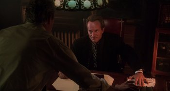 Movie still from “Hard Target” (1993), directed by John Woo – A man sitting at a table in front of another man; Medium shot, Over the shoulder angle