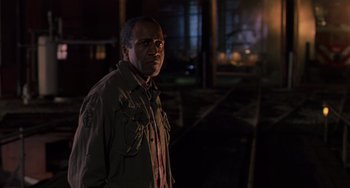 Movie still from “Hard Target” (1993), directed by John Woo – A man standing in the dark near a train track; Medium shot, Low angle