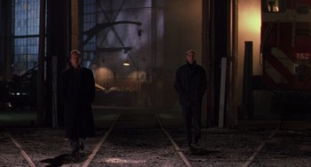 Movie still from “Hard Target” (1993), directed by John Woo – Two men are standing in the middle of a train yard; Wide shot, Low angle