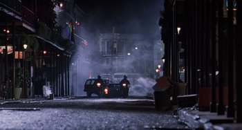 Movie still from “Hard Target” (1993), directed by John Woo – A car driving down a street at night with smoke coming out of it; Extreme Wide shot, Low angle
