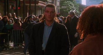 Movie still from “Hard Target” (1993), directed by John Woo – A man with long hair is walking down the street; Close Up shot, Over the shoulder angle