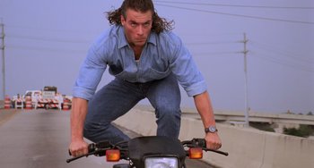 Movie still from “Hard Target” (1993), directed by John Woo – A man riding a motorcycle down a street; Medium shot, Low angle