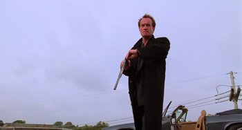 Movie still from “Hard Target” (1993), directed by John Woo – A man holding a gun while standing next to a car; Medium shot, Low angle