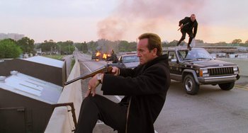 Movie still from “Hard Target” (1993), directed by John Woo – A man sitting on a bench with a gun in his hand; Medium shot, Low angle