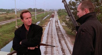 Movie still from “Hard Target” (1993), directed by John Woo – Two men standing next to each other on train tracks; Medium shot, Over the shoulder angle
