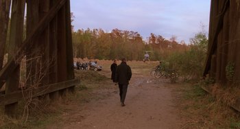 Two men walking down a dirt road near a forest