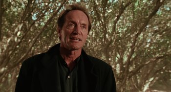 Movie still from “Hard Target” (1993), directed by John Woo – An older man in a black shirt and a black jacket; Close Up shot, Low angle