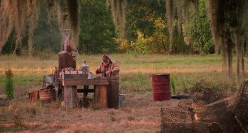Movie still from “Hard Target” (1993), directed by John Woo – A man sitting at a table in the middle of a field; Wide shot, High angle