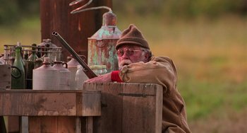 Movie still from “Hard Target” (1993), directed by John Woo – An old man sitting on top of a wooden box; Medium shot, Over the shoulder angle