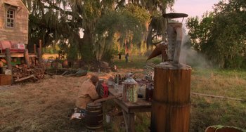 Movie still from “Hard Target” (1993), directed by John Woo – A man sitting at a wooden table in a field; Extreme Wide shot, High angle