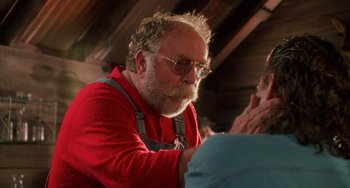 Movie still from “Hard Target” (1993), directed by John Woo – An older man with a beard wearing glasses and a red shirt; Close Up shot, Over the shoulder angle