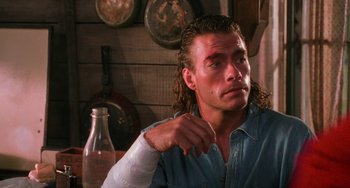 Movie still from “Hard Target” (1993), directed by John Woo – A person sitting in a room near a bottle; Close Up shot, Over the shoulder angle