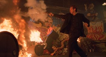 Movie still from “Hard Target” (1993), directed by John Woo – A man holding a sword near a burning statue; Medium shot, Low angle
