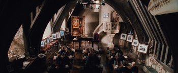 Movie still from “Harry Potter and the Chamber of Secrets” (2002), directed by Chris Columbus – A group of people sitting in a room with paintings on the walls; Extreme Wide shot, High angle