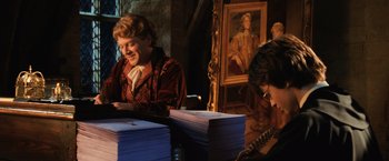 Movie still from “Harry Potter and the Chamber of Secrets” (2002), directed by Chris Columbus – Two people sitting in front of a stack of papers; Medium shot, High angle