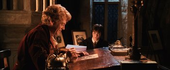 Movie still from “Harry Potter and the Chamber of Secrets” (2002), directed by Chris Columbus – Two people sitting at a wooden table in front of a window; Medium shot, Over the shoulder angle