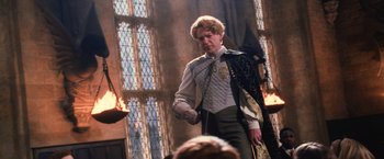 Movie still from “Harry Potter and the Chamber of Secrets” (2002), directed by Chris Columbus – A man in a suit and tie standing in front of stained glass windows; Medium shot, Low angle