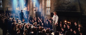 Movie still from “Harry Potter and the Chamber of Secrets” (2002), directed by Chris Columbus – A group of people sitting in front of a group of students; Wide shot, High angle
