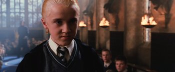 Movie still from “Harry Potter and the Chamber of Secrets” (2002), directed by Chris Columbus – A young man with blonde hair is standing in front of a group of other young men; Close Up shot, Low angle