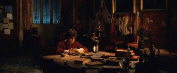 Movie still from “Harry Potter and the Chamber of Secrets” (2002), directed by Chris Columbus – A person sitting at a table reading a book; Medium shot, High angle