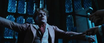 Movie still from “Harry Potter and the Chamber of Secrets” (2002), directed by Chris Columbus – A man wearing a suit and tie standing in front of stained glass windows; Medium shot, Low angle