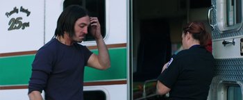 Movie still from “Asking for It” (2021), directed by Eamon O'Rourke – A man standing next to another man in front of a bus; Medium shot, Over the shoulder angle