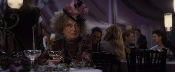 Movie still from “Harry Potter and the Deathly Hallows: Part 1” (2010), directed by David Yates – An older woman wearing a fancy hat at an event; Close Up shot, Over the shoulder angle