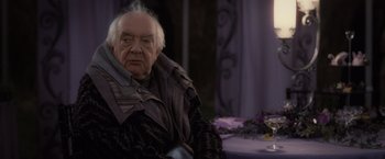 Movie still from “Harry Potter and the Deathly Hallows: Part 1” (2010), directed by David Yates – An older man sitting at a table in front of a purple curtain; Close Up shot, Over the shoulder angle