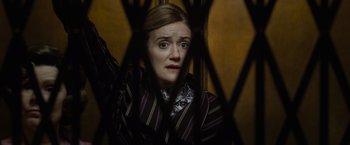Movie still from “Harry Potter and the Deathly Hallows: Part 1” (2010), directed by David Yates – A woman in a striped suit looking at the camera through a fence; Close Up shot, Low angle