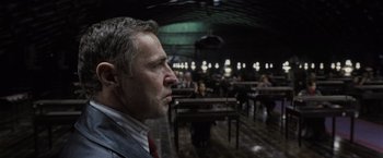 Movie still from “Harry Potter and the Deathly Hallows: Part 1” (2010), directed by David Yates – A man looking into the distance in a room filled with tables; Close Up shot, Over the shoulder angle