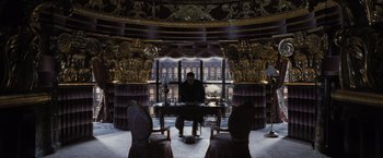 Movie still from “Harry Potter and the Deathly Hallows: Part 1” (2010), directed by David Yates – A man sitting at a table in a room with gold decorations; Wide shot, High angle