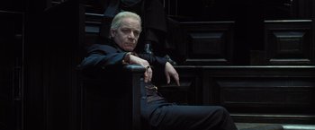 Movie still from “Harry Potter and the Deathly Hallows: Part 1” (2010), directed by David Yates – A man sitting in a chair with his hands on his knees; Medium shot, Low angle