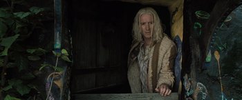 Movie still from “Harry Potter and the Deathly Hallows: Part 1” (2010), directed by David Yates – A man with long white hair standing next to a wooden table; Medium shot, Low angle