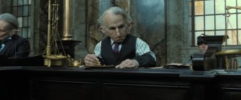 Movie still from “Harry Potter and the Deathly Hallows: Part 2” (2011), directed by David Yates – An old man sitting at a table writing on a piece of paper; Medium shot, Low angle